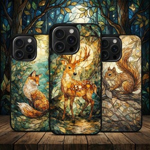 Könnte beinhalten: Drei Handyhüllen mit Naturmotiven. Eine Hülle zeigt einen Fuchs, eine andere einen Hirsch und die dritte ein Eichhörnchen. Die Hüllen haben einen Buntglasstil mit Wald- und Mondhintergründen. Die Hüllen werden auf einer Holzoberfläche präsentiert.