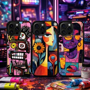 May include: Three phone cases with colorful abstract art designs. The cases feature a robot, a woman with a flower, and a person with sunglasses. Paint tubes and a palette with paint are in the foreground.