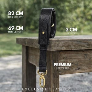 May include: Black leather bag strap with gold-colored hardware. The strap has a maximum length of 82 cm (32.3 inches), a minimum length of 69 cm (27.2 inches), and a width of 3 cm (1.2 inches). The text "PREMIUM HARDWARE" and "EXCLUSIVE LEATHER" are visible.