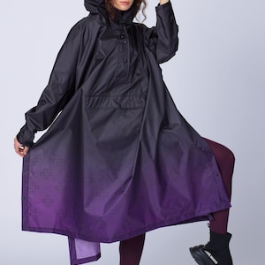 May include: A black hooded poncho-style raincoat with a purple ombre effect at the hem. The raincoat features a front pocket and a cross pattern on the purple section. The model is wearing black ankle boots.