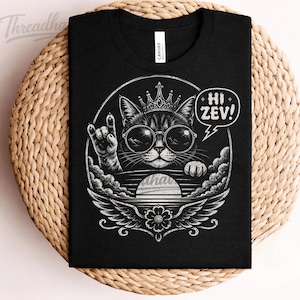 Könnte beinhalten: Schwarzes T-Shirt mit einer Grafik einer Katze mit Sonnenbrille und Krone, die eine Rock'n'Roll-Handbewegung macht. Das Design enthält den Text "Hi Zev!" in einer Sprechblase und eine kreisförmige Grafik mit Flügeln und einer Blume.