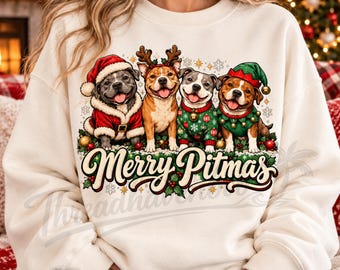 May include: A cream-colored sweatshirt featuring a graphic of four pit bull dogs dressed in holiday attire, including a Santa suit, reindeer antlers, a green sweater, and an elf hat. The text Merry Pitmas is printed below the dogs.