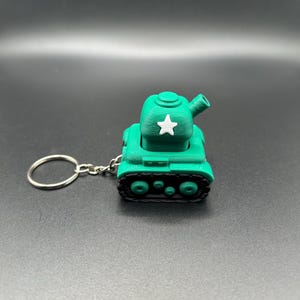 May include: A green 3D-printed tank keychain with a white star on the turret. The tank has black treads and a silver keyring attached. The toy tank is a novelty item.
