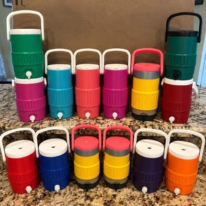 May include: A selection of brightly coloured beverage coolers in shades of green, pink, blue, red, yellow, and orange. Each cooler has a white handle and a tap for dispensing drinks. The coolers are designed to keep drinks cool.