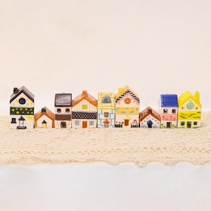 May include: A row of colorful ceramic miniature houses. Each house has a unique design, with varying roof styles, window shapes, and decorative details. The houses are painted in a variety of colors, including yellow, blue, brown, and white.