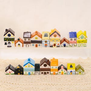 May include: A collection of miniature ceramic houses in various colors and designs. The houses feature details like windows, doors, and decorative patterns. Some have chimneys and unique roof styles, creating a charming village scene.