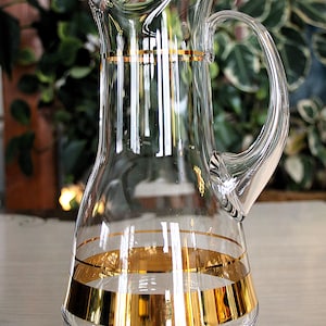 Peut inclure: Pichet en verre transparent avec une anse incurvée et un bec verseur. Le pichet est orné de bandes dorées autour de la base et près du haut. Un objet classique pour servir des boissons.