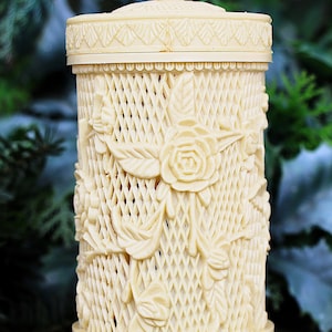 Peut inclure: Conteneur décoratif de couleur ivoire avec un couvercle, présentant un motif en treillis et des sculptures florales en relief. Le conteneur a une forme cylindrique avec une base et un couvercle surmonté d'un fleuron en forme de fleur.
