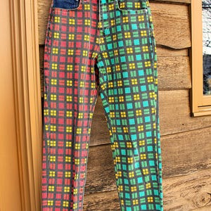 May include: High-waisted denim jeans with a distinctive plaid pattern. The jeans have a dark blue denim waistband. The legs are split, with one side showing a red and yellow plaid, and the other a green and yellow plaid.