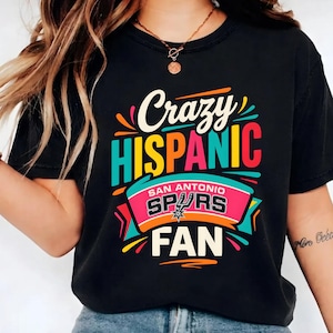 Puede incluir: Camiseta negra con la frase "Crazy Hispanic San Antonio Spurs Fan" en un diseño colorido. El diseño incluye el logotipo de los Spurs, ideal para los aficionados al baloncesto.