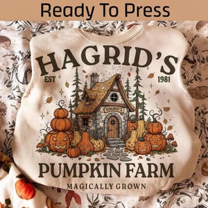 Pode incluir: Uma camisola cor de creme com um gráfico castanho de uma cabana e o texto HAGRID'S EST 1981 PUMPKIN FARM MAGICALLY GROWN. O design inclui várias abóboras cor de laranja, lanternas, pinheiros e folhas de outono a cair no estampado.
