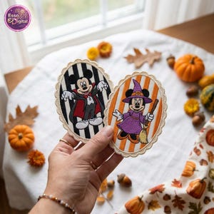 May include: Two oval embroidered patches with scalloped edges. One patch features Mickey Mouse dressed as a vampire against black and white stripes. The other patch features Minnie Mouse dressed as a witch against orange and white stripes.