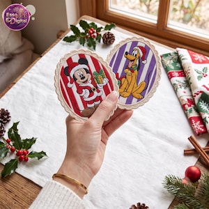 May include: Two oval-shaped fabric coasters with scalloped edges. One coaster features Mickey Mouse in a Santa suit holding a gift against red and white stripes. The other coaster shows Pluto wearing a Santa hat against purple and white stripes.