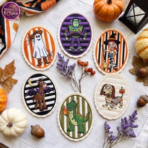 May include: Six oval-shaped embroidered patches featuring cartoon characters in Halloween costumes. The designs include a ghost, a space ranger, a cowgirl witch, a winged horse, a dinosaur holding a flame, and a mummy dog on striped backgrounds.