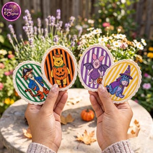May include: Four oval-shaped decorative coasters featuring Winnie the Pooh characters in Halloween costumes. Tigger is a pirate, Pooh is a pumpkin, Piglet is a bat, and Eeyore is a wizard. Each coaster has a scalloped edge and striped background.