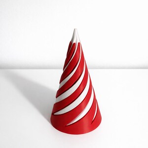 May include: A red and white party hat with a spiral design. The cone-shaped hat has alternating red and white stripes, creating a visually striking pattern. The hat is made of a rigid material and stands upright on a white surface.