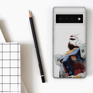 May include: A white phone case featuring a colorful illustration of a robot. The robot has a white head, red accents, and blue and yellow details. A black pencil and a notepad with a grid pattern are also visible.