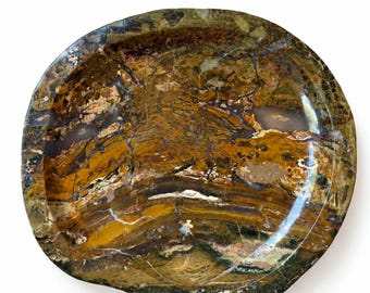 Pode incluir: Uma tigela circular de pedra com uma superfície polida com padrões intrincados e rodopiantes em tons de verde floresta profundo, ocre dourado, castanho escuro e creme. A textura mineral natural apresenta faixas orgânicas variadas.