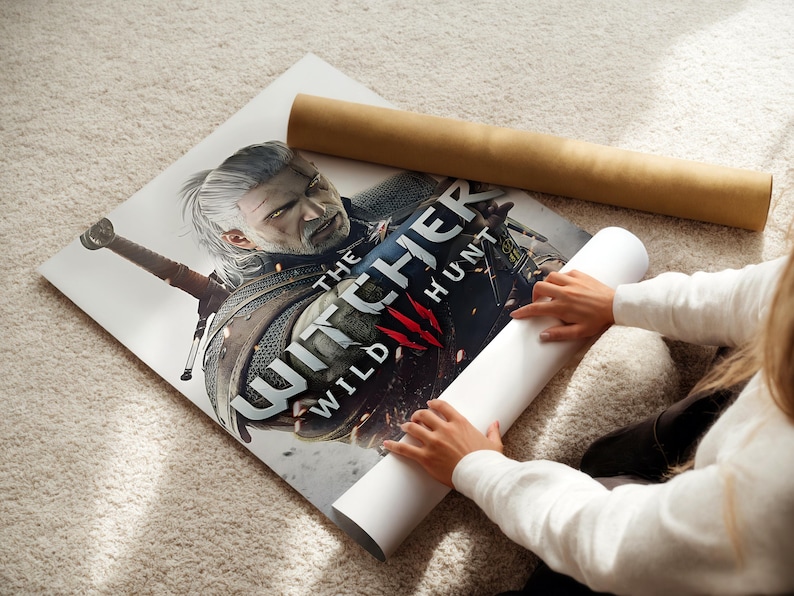 A person is holding a poster of a character from the video game The Witcher, which features a sword and a detailed illustration of the character.
