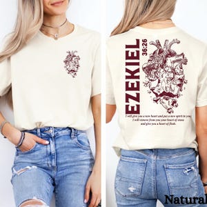 Könnte beinhalten: Cremefarbenes T-Shirt mit einem weinroten anatomischen Herz-Motiv auf Vorder- und Rückseite. Auf der Rückseite des Shirts steht das Wort "EZEKIEL" vertikal, mit der Schriftstelle "36:26" und einem zugehörigen Zitat. Das Shirt ist aus weichem Material.