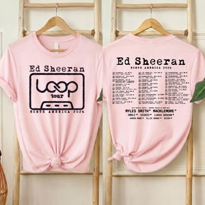 May include: A light pink short-sleeve t-shirt featuring a black graphic of a cassette tape with the text Ed Sheeran Loop Tour North America 2026 on the front and a list of tour dates and locations printed on the back in black ink.