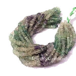Könnte beinhalten: Ein Bündel mehrfarbiger Fluorite-Edelsteinperlen. Die Perlen sind quadratisch und aufgereiht und zeigen Farbtöne von Grün, Lila und Klar. Die Perlen befinden sich auf weißem Hintergrund. Der Text "JewelryGemsIndi" ist sichtbar.