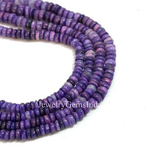 May include: Close-up of strands of purple gemstone beads. The beads are small, round, and have a slightly irregular shape. The color varies from light lavender to deep violet, with some pinkish hues. The text "JewelryGemsInda" is visible.