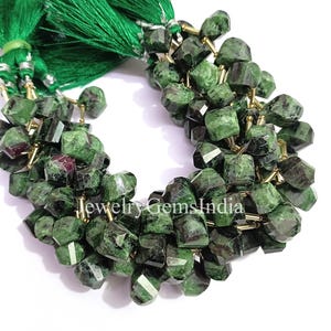 Könnte beinhalten: Strang aus facettierten grünen und dunkelroten Edelsteinperlen. Die Perlen sind mit goldfarbenem Draht aufgefädelt und mit einer grünen Quaste versehen. Die Perlen sind eine Mischung aus dunkelgrün und rot.