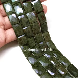 May include: Close-up of strands of olive green gemstone beads. The beads are rectangular with faceted surfaces, creating a sparkling effect. The text "Jewelry GemsIndia" is visible at the bottom.