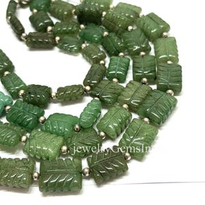 May include: A necklace of green gemstone beads carved in a leaf design. The beads are strung together with small silver-colored beads. The necklace is displayed on a white background. The text "jewelryGemsIn" is visible.
