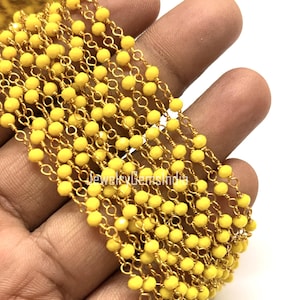 Könnte beinhalten: Nahaufnahme von Strängen gelber Perlenketten mit goldfarbenen Gliedern. Die Perlen sind klein und rund, und die Kette wird in einer Hand gehalten. Der Text "jewelrygemsindia" ist auf dem Bild sichtbar.