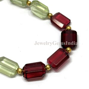 May include: A beaded necklace featuring alternating rectangular faceted beads in translucent light green and deep red. Small, round, metallic gold-colored spacer beads are placed between each rectangular bead. The text JewelryGemsIndia is visible.
