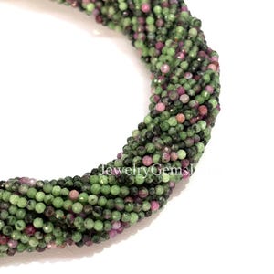 Könnte beinhalten: Nahaufnahme eines Strangs Edelsteinperlen. Die Perlen sind eine Mischung aus Grün und Rosa, mit einem facettierten Schliff, der das Licht einfängt. Der Text "Jewelry Gems" ist sichtbar.