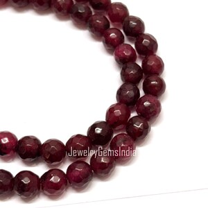 Könnte beinhalten: Nahaufnahme einer Kette aus facettierten, tiefroten Edelsteinperlen. Die Perlen sind rund und haben mehrere Facetten, wodurch ein funkelnder Effekt entsteht. Der Text "JewelryGemsIndia" ist sichtbar.