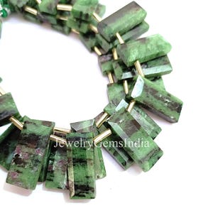 Op de afbeelding: Close-up van een streng groene en zwarte rechthoekige edelsteen kralen. De kralen zijn geregen met goudkleurige metalen pinnen. De tekst "JewelryGemsIndia" is zichtbaar onderaan de afbeelding.