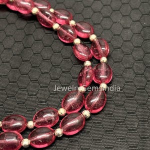 Könnte beinhalten: Nahaufnahme einer Halskette mit ovalen, durchscheinenden rosa Perlen, die durch silberfarbene Abstandshalter getrennt sind. Die Perlen haben eine glänzende Oberfläche. Der Text "jewelrygemsindia" ist sichtbar.
