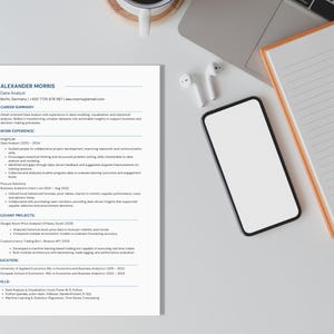 Op de afbeelding: Een cv met de titel "ALEXANDER MORRIS Data Analyst" met contactgegevens, carrière-overzicht, werkervaring, relevante projecten, opleiding en vaardigheden. Een smartphone, notitieboek, pen, oortelefoons en laptop liggen ook op het witte oppervlak.