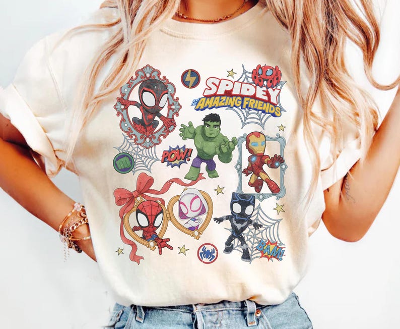 以下が含まれることがあります： クリーム色のTシャツ。ハルク、アイアンマン、ブラックパンサーなどの「スパイディとすごいなかまたち」のキャラクターのグラフィックプリントが施されており、「Spidey and His Amazing Friends」の文字とクモの巣や星のアクセントが描かれています。