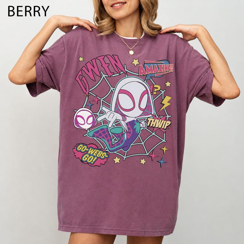 May include: A berry-colored short-sleeve t-shirt featuring a graphic of the character Gwen Stacy in a spiderweb design. The print includes the text GWEN, AMAZING, THWIP, and GO-WEBS-GO, along with yellow stars and lightning bolt accents on the front.