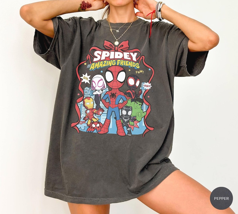 May include: A charcoal grey short-sleeve t-shirt featuring a graphic print of Spidey and His Amazing Friends. The design includes Spider-Man, Ghost-Spider, Iron Man, Black Panther, and Hulk, with the text "SPIDEY AND HIS AMAZING FRIENDS".