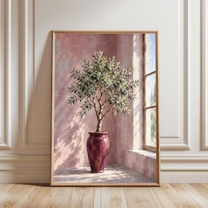 Op de afbeelding: Een ingelijste muurkunstprint met een olijfboom met donkere vruchten in een diepbordeauxrode keramische vaas. De scène bevindt zich tegen een roze muur met textuur in een hoek naast een raam, waarbij zonlicht schaduwen op de vloer werpt.
