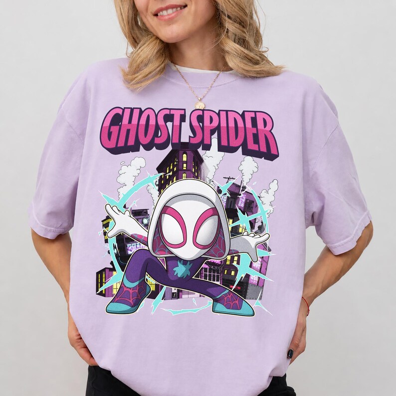May include: A light purple t-shirt featuring a Ghost Spider graphic. The design includes the text "GHOST SPIDER" in pink and white, along with an illustration of the character in a dynamic pose against a cityscape background.