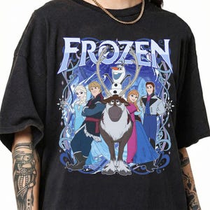 May include: A black short-sleeve t-shirt featuring a large graphic print of the characters Elsa, Kristoff, Sven, Olaf, Anna, and Hans from the movie Frozen. The text Frozen is printed in large blue letters above the characters with blue swirls.