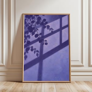 May include: A rectangular wall art print in a light wood frame featuring a purple background with a dark purple shadow cast by a window frame and leafy plant branches. The artwork displays a cross-shaped window pane shadow and foliage.