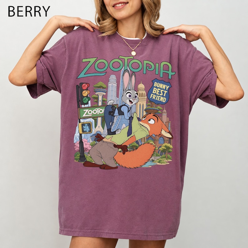 May include: A berry-colored short-sleeve t-shirt featuring a graphic print of the characters Judy Hopps and Nick Wilde from Zootopia. The design includes the text Zootopia and Bunny Best Friend, set against a colorful city skyline background.
