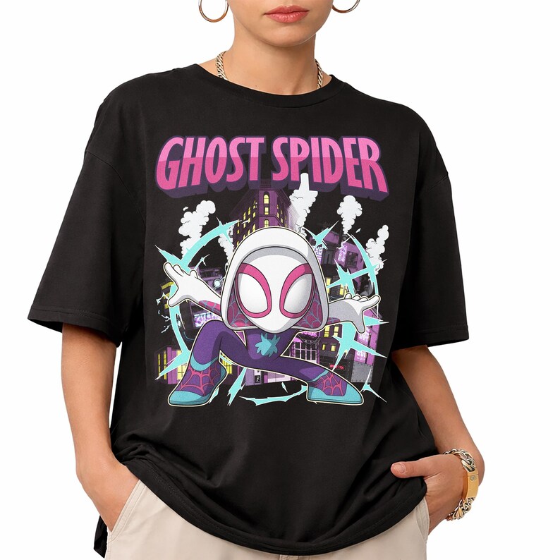 May include: Black t-shirt featuring a Ghost Spider graphic. The design includes a cartoon illustration of Ghost Spider in a dynamic pose, set against a cityscape background. The text "Ghost Spider" is displayed in pink and purple.