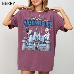 May include: Berry-colored t-shirt featuring the text "Meet me in Arendelle" above a graphic of a castle, reindeer, and Olaf the snowman. The shirt has short sleeves and a relaxed fit, perfect for casual wear.