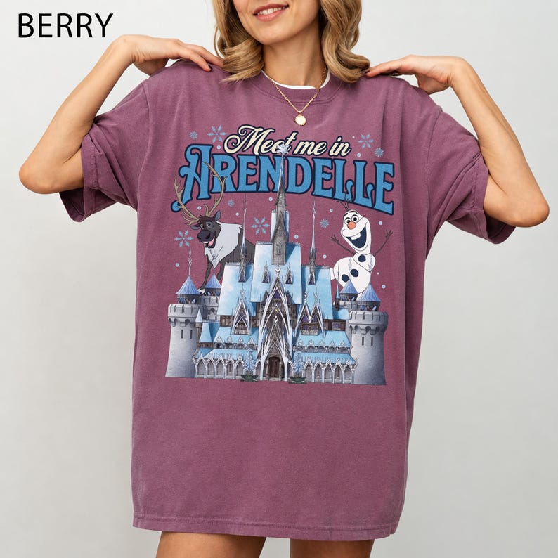 May include: Berry-colored t-shirt featuring the text "Meet me in Arendelle" above a graphic of a castle, reindeer, and Olaf the snowman. The shirt has short sleeves and a relaxed fit, perfect for casual wear.