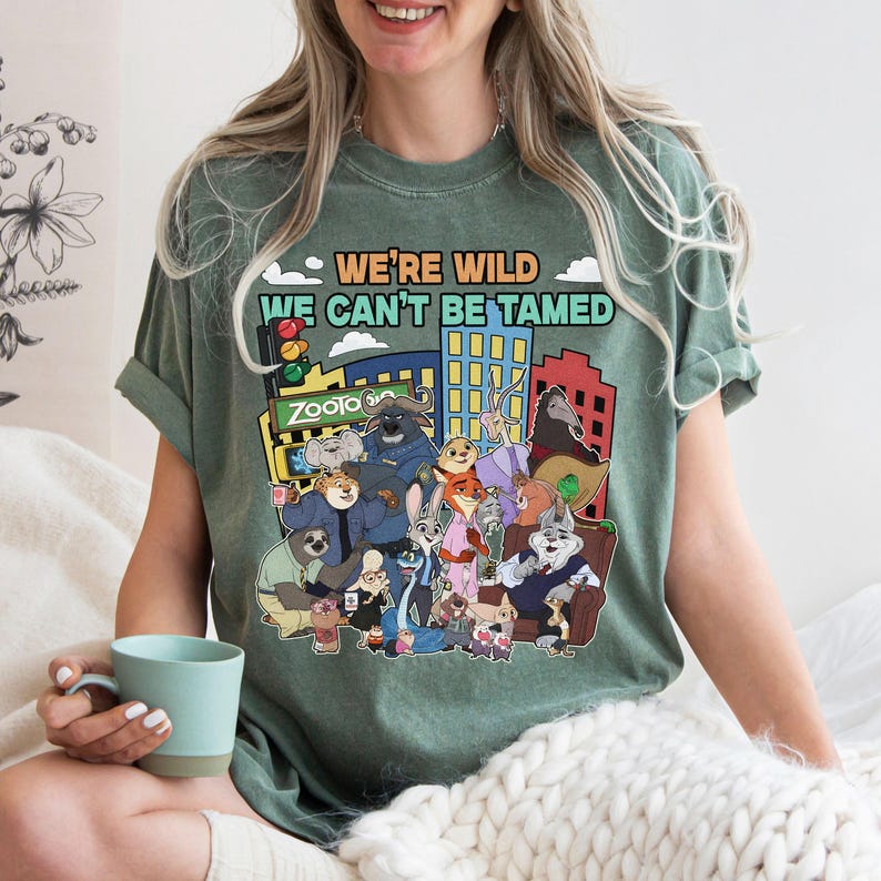 May include: Green t-shirt featuring a colorful graphic of characters from the animated movie Zootopia, with the text "WE'RE WILD WE CAN'T BE TAMED". The design includes a cityscape and various animal characters.