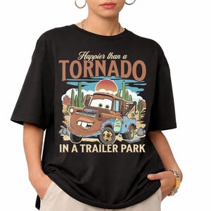 May include: Black t-shirt with a cartoon image of Mater from the film Cars, and the text "Happier than a Tornado in a Trailer Park." The design includes a desert landscape with cacti and a setting sun.